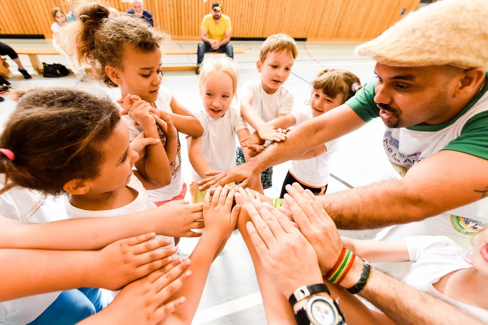 Gruppenspiel mit Kindern, die ihre Hände zum gemeinsamen Aufeinandertreffen heben, unter Anleitung eines Erwachsenen.