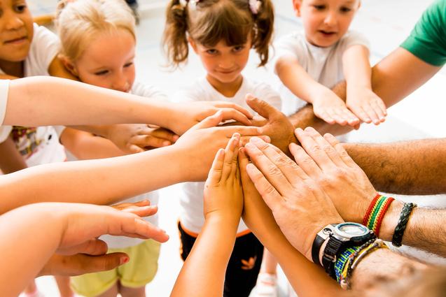 Kinder und Erwachsene legen ihre Hände in einem Kreis zusammen, symbolisieren Zusammenarbeit und Gemeinschaft.