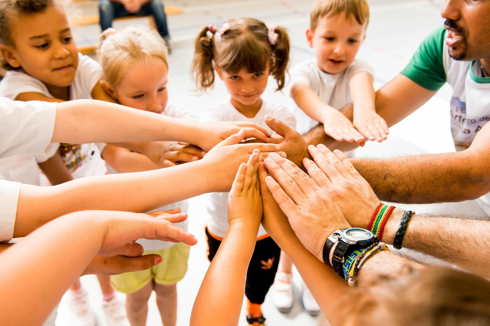 Kinder und Erwachsene legen ihre Hände in einem Kreis zusammen, symbolisieren Zusammenarbeit und Gemeinschaft.