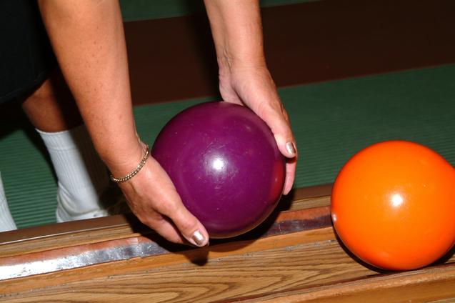 Nahaufnahme einer Hand, die eine lilafarbene Kugel über einer Holzfläche hält, neben einer orangefarbenen Kugel.