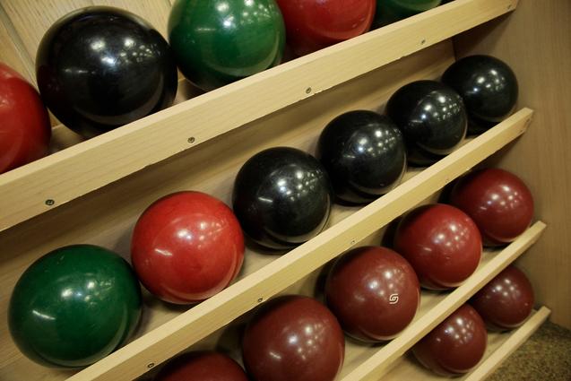 Regal mit bunten Bowlingkugeln in Rot, Grün, Schwarz und Braun, ordentlich gestapelt auf Holzregalen.