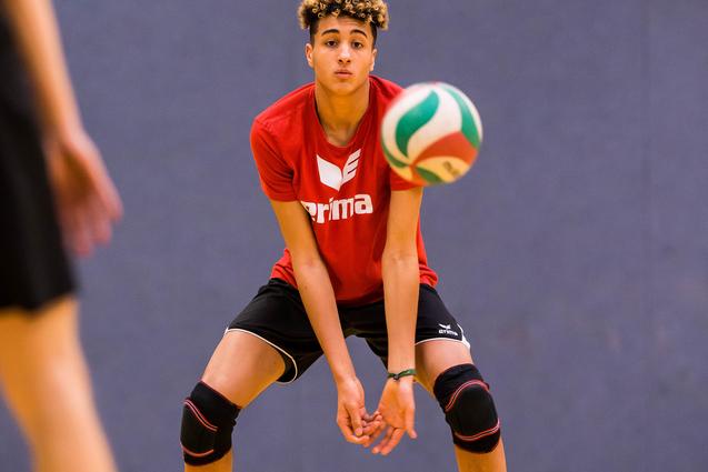 Junger Volleyballspieler in rotem Shirt bereit, einen bunten Volleyball zu empfangen, auf einem Holzsportboden.