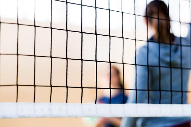 Nahaufnahme eines Volleyballnetzes mit unscharfen Spielern im Hintergrund in einer Sporthalle.